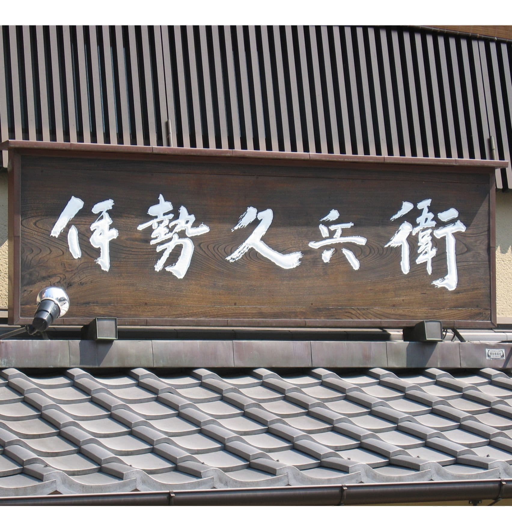 瓦の上に木の看板、白い文字で老舗の和菓子屋の看板