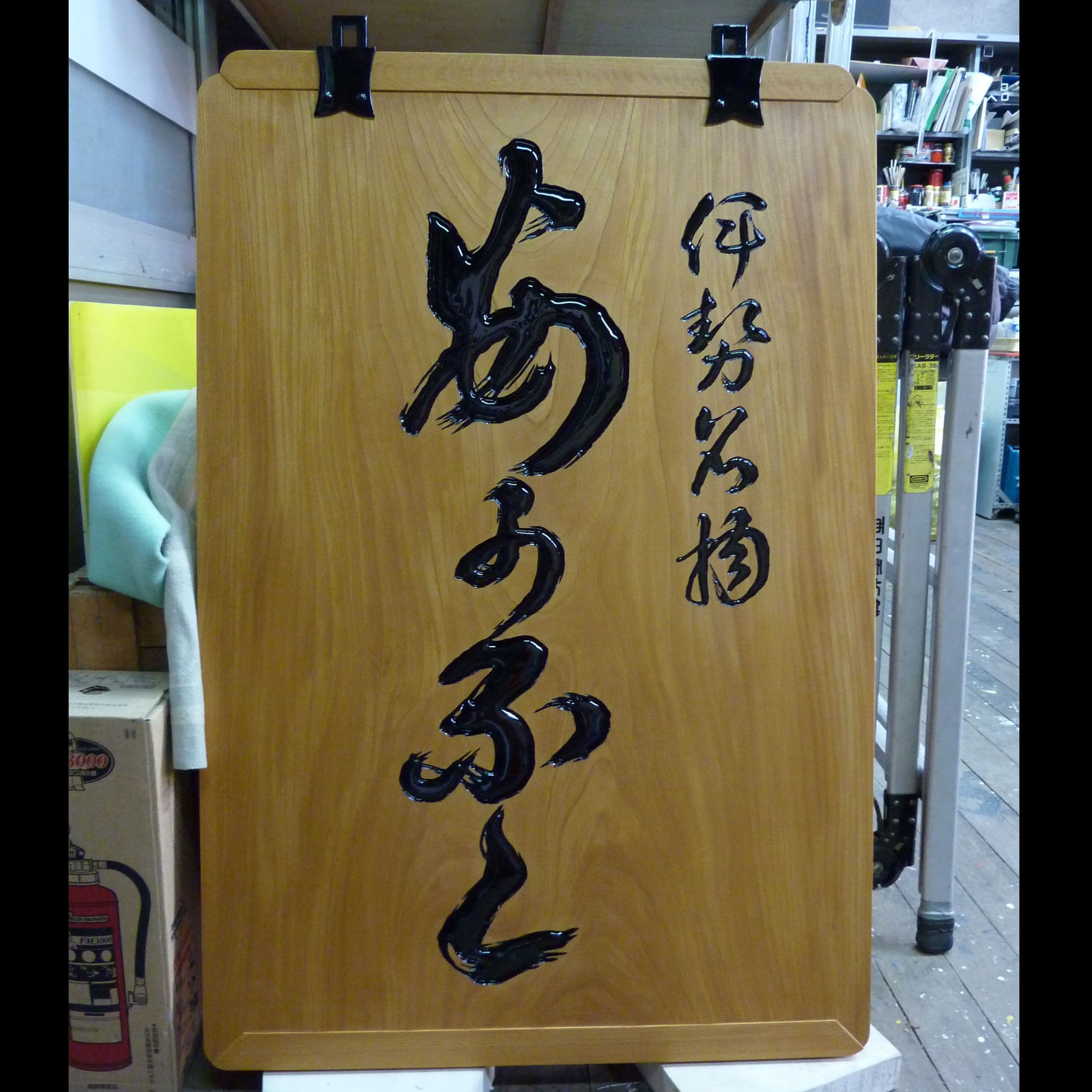 吊下げの金具が着いた木の看板で文字は彫刻され黒色、伝統的な看板