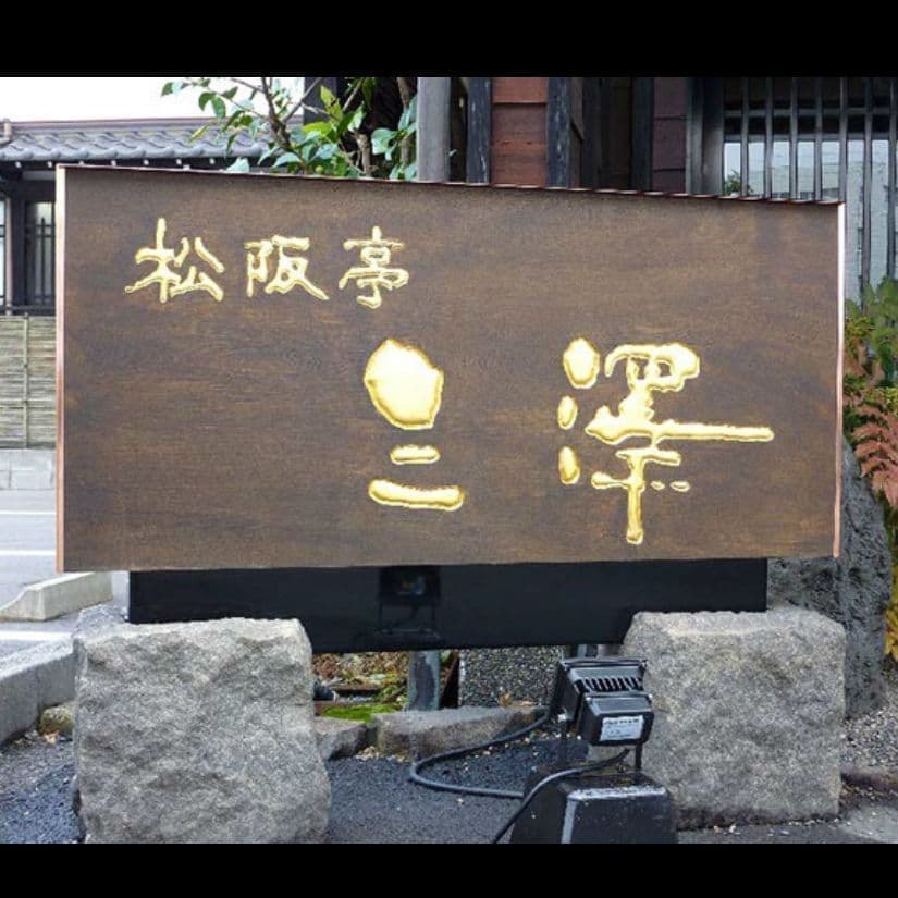 石の台の上に乗った木の板に金箔の文字が彫刻されているしゃぶしゃぶ店の看板
