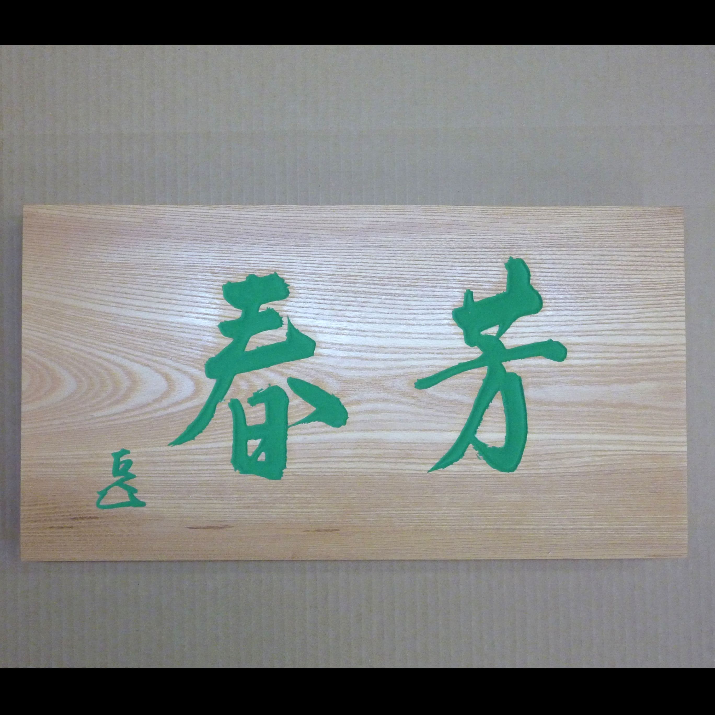 ケヤキの木の板に緑の文字で揮毫と花押が書いてある彫刻看板、扁額